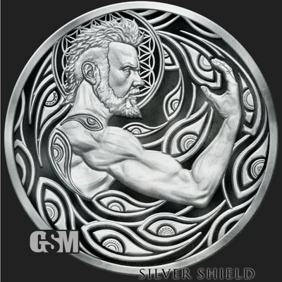 A circular silver-toned medallion or coin featuring a muscular bearded male figure in profile, surrounded by ornate flowing wave-like patterns. The piece is shown on a dark background with a visible 'GSM' mark at lower left and the text 'SILVER SHIELD' at lower right.